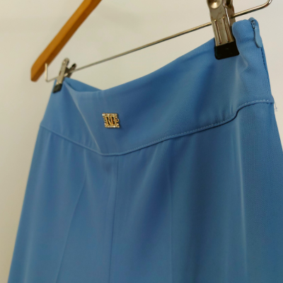 saia azul clara com símbolo metálico SRE pendurada em cabide de madeira