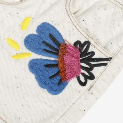 Peça de vestuário branca com bordado colorido de flor e pequenas manchas pretas