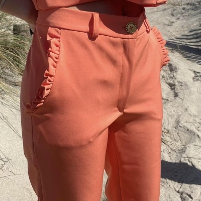 Calças de tecido salmão com folhos ao ar livre na areia