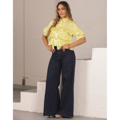 Mulher com blusa amarela de folhos e calças de ganga azul escura de perna larga num espaço interior