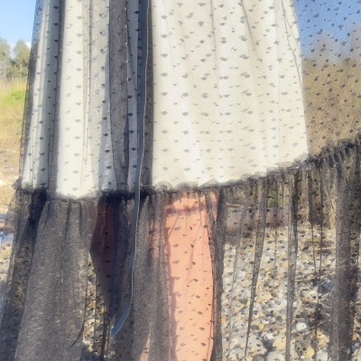 vestido preto transparente com pontos e franjas, sobre vestido branco, fundo exterior com pedras