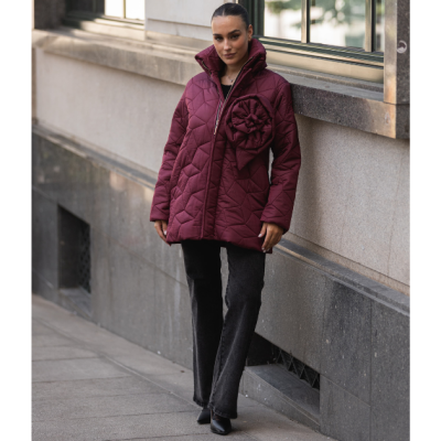 Mulher com casaco acolchoado vinho com flor decorativa e calças pretas na rua