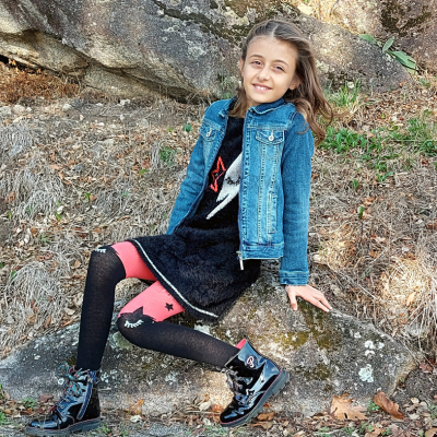 Menina com casaco de ganga e vestido preto sentada numa rocha ao ar livre