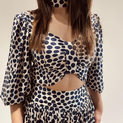 Conjunto de roupa branco com bolinhas azuis escuras, top e saia com volantes e acessório no pescoço.