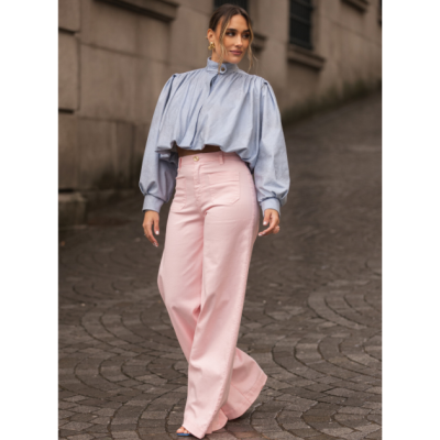 Mulher a usar blusa azul clara de gola alta e calças rosa largas na rua