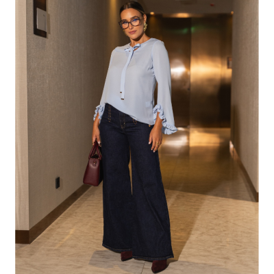 Mulher com blusa azul clara e calças largas de ganga azul escuro num corredor interior