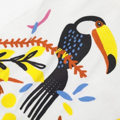 Estampa de tecido branco com desenho de tucano colorido e folhas.