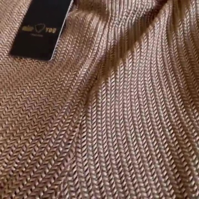 Peça de roupa dourada em malha com padrão em chevron, com etiqueta da marca visível.