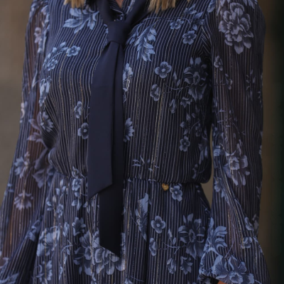 Vestido feminino azul com padrão de riscas e flores, mangas transparentes e laço no pescoço.
