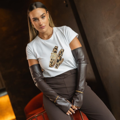 Mulher com t-shirt branca com estampado de relógio, luvas castanhas de pele e calças castanhas