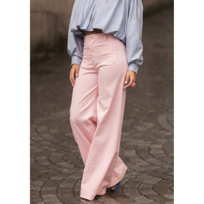 Calças largas rosa com blusa azul clara e sapatos azuis num pavimento de calçada cinzenta