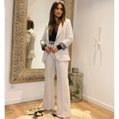 Mulher com fato branco de blazer e calças largas, com detalhe animal print nas mangas, no interior de uma divisão com espelho grande e chão de madeira.