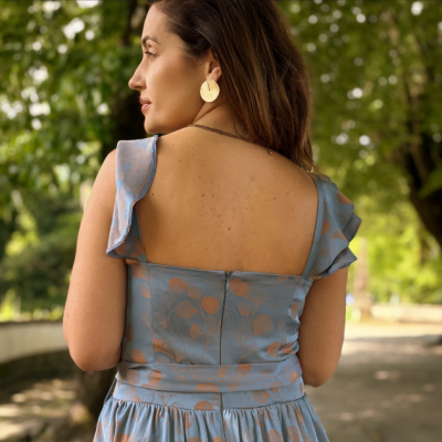Vestido azul claro com padrão floral e mangas com folhos, visto pelas costas