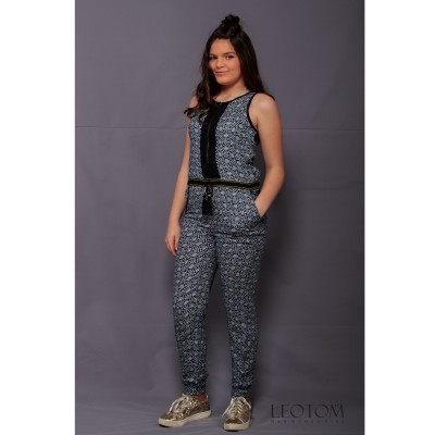 Mulher a usar macacão preto e branco com padrão geométrico e cinto preto, sapatos dourados, fundo cinzento