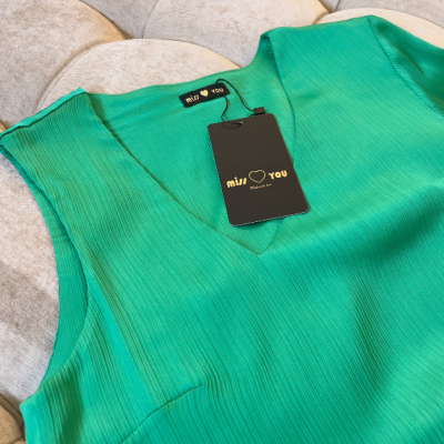 Blusa verde canelada com decote em V e etiqueta 'miss love you' sobre almofada bege