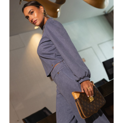 Mulher vestindo fato azul macio segurando mala castanha com padrão Louis Vuitton em ambiente interior