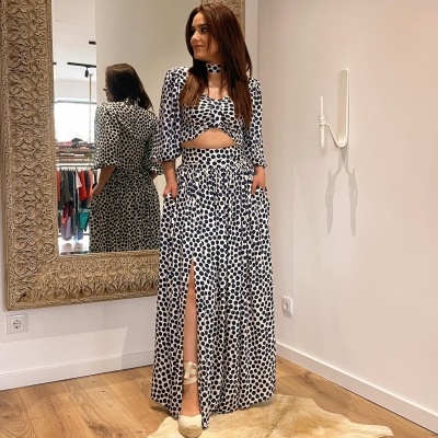 Conjunto feminino branco com bolinhas negras com top e saia longa fendida, sapatos bege, interior com espelho e chão de madeira