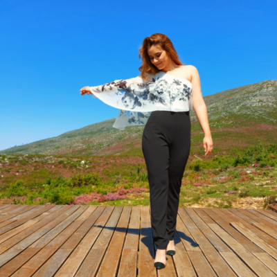 Mulher com calças pretas e blusa branca com flores num ambiente natural ao ar livre