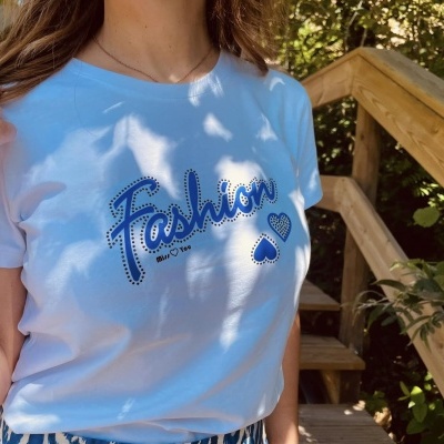 T-shirt branca com texto Fashion azul e corações, exterior com madeira e plantas