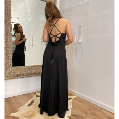 Vestido preto comprido com alças cruzadas nas costas em sala branca com espelho e tapete de pele