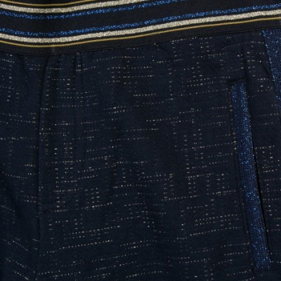 Detalhe de calças ou saia azul escuro com cintura riscada dourada e branca e bolsos