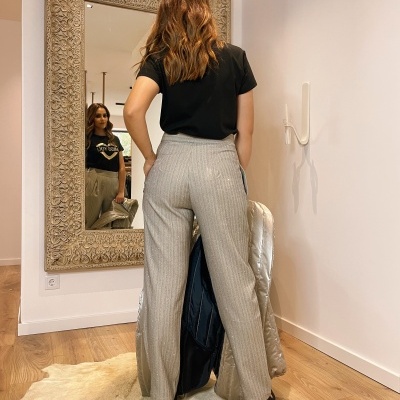 Mulher vestindo calças cinza e t-shirt preta, refletida num espelho grande