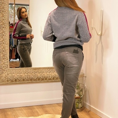 Mulher de costas a usar casaco cinzento com risca vermelha e calças cinzentas em frente a espelho