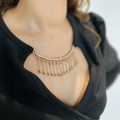 Colar dourado com correntes e bolas usado sobre blusa preta