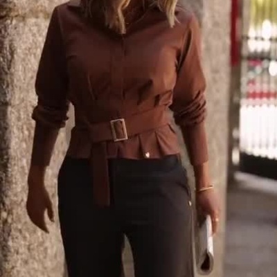 Mulher com camisa castanha e calças pretas numa rua com colunas de pedra