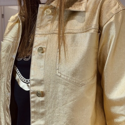 Casaco dourado metálico com bolso frontal e botões de metal sobre t-shirt preta com estampado.