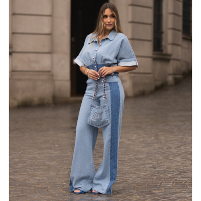 Mulher com roupa de ganga azul clara e mala de corrente azul com letras MY, em rua de pedra