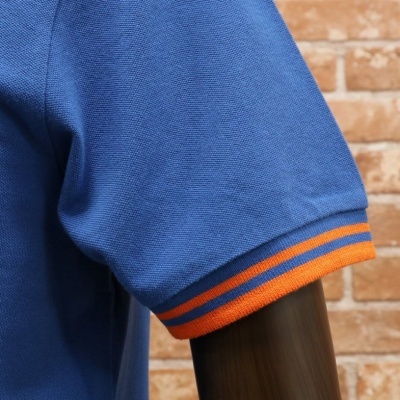 Manga de t-shirt ou polo azul com riscas laranja na manga diante de parede de tijolos