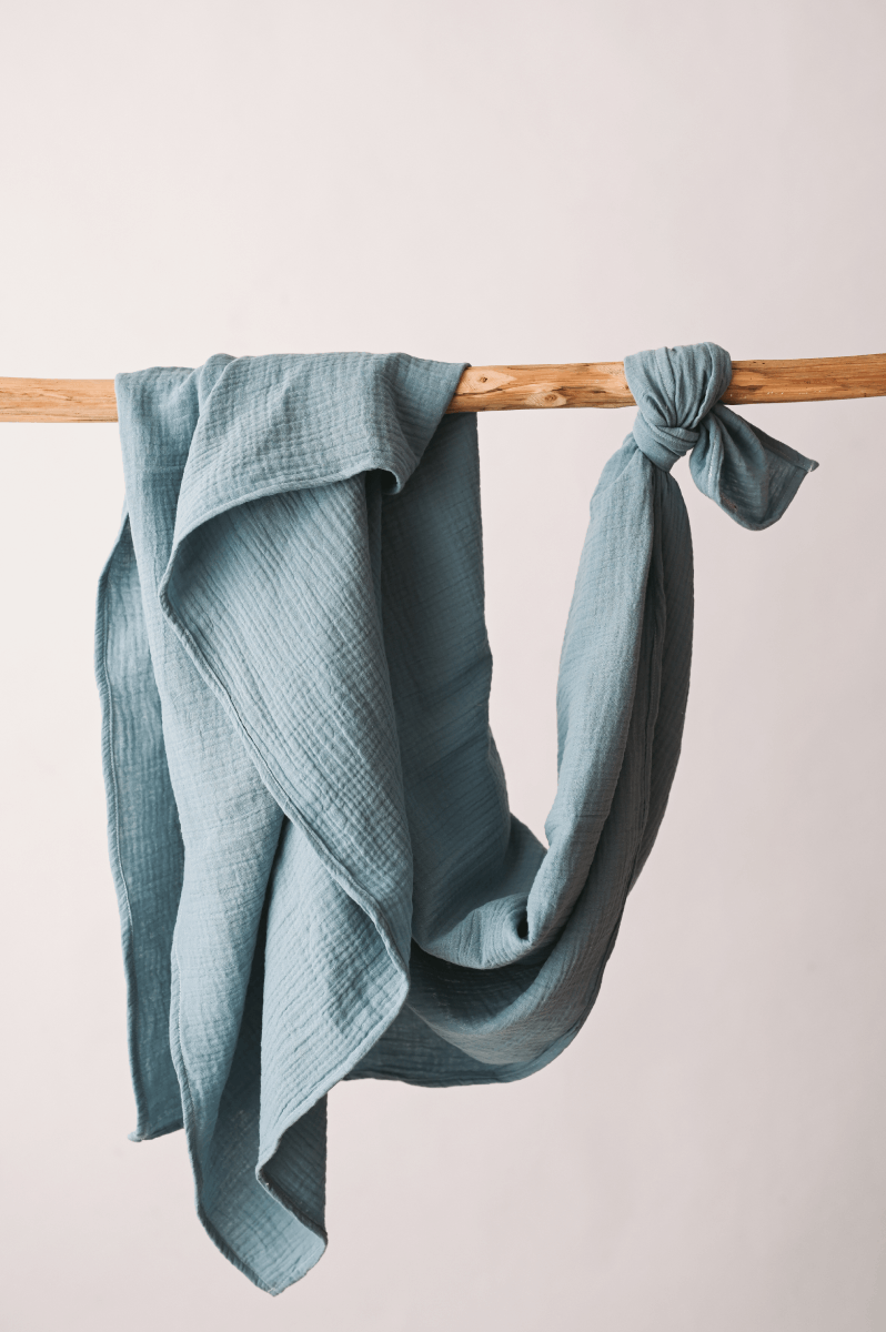 Fralda Swaddle Lenço azul claro com textura pendurado em pau de madeira