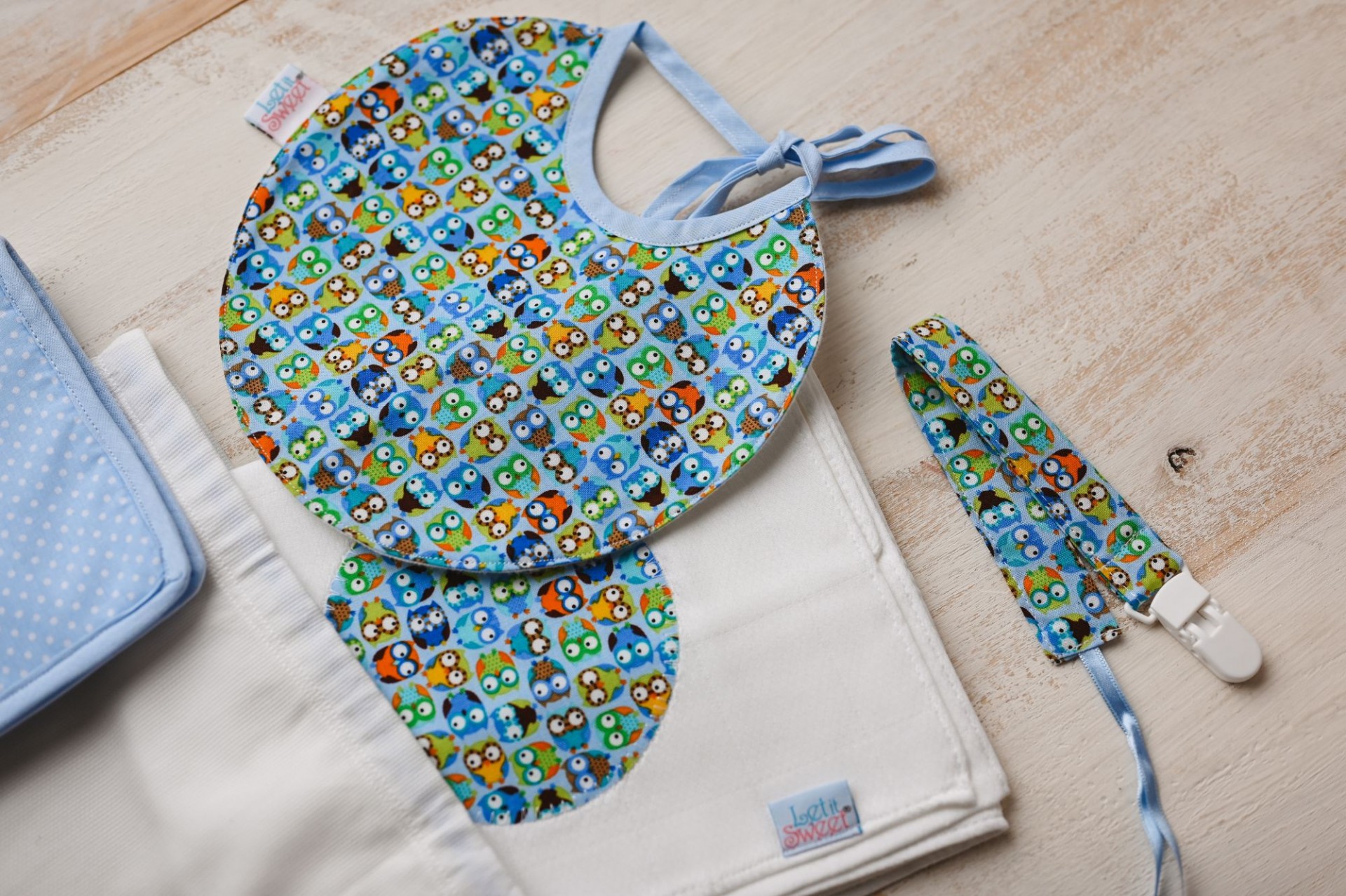 Conjunto de essenciais Babete e chucha para bebé com padrão colorido de animais sobre tecido branco e fundo de madeira clara