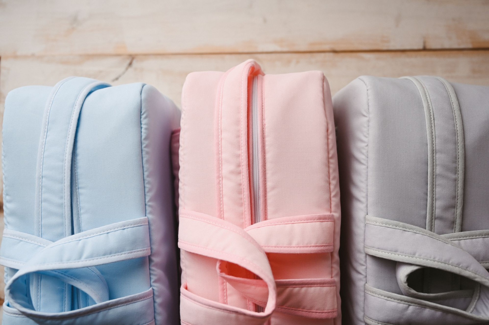 Mala de maternidade Três mochilas coloridas alinhadas sobre uma mesa de madeira clara