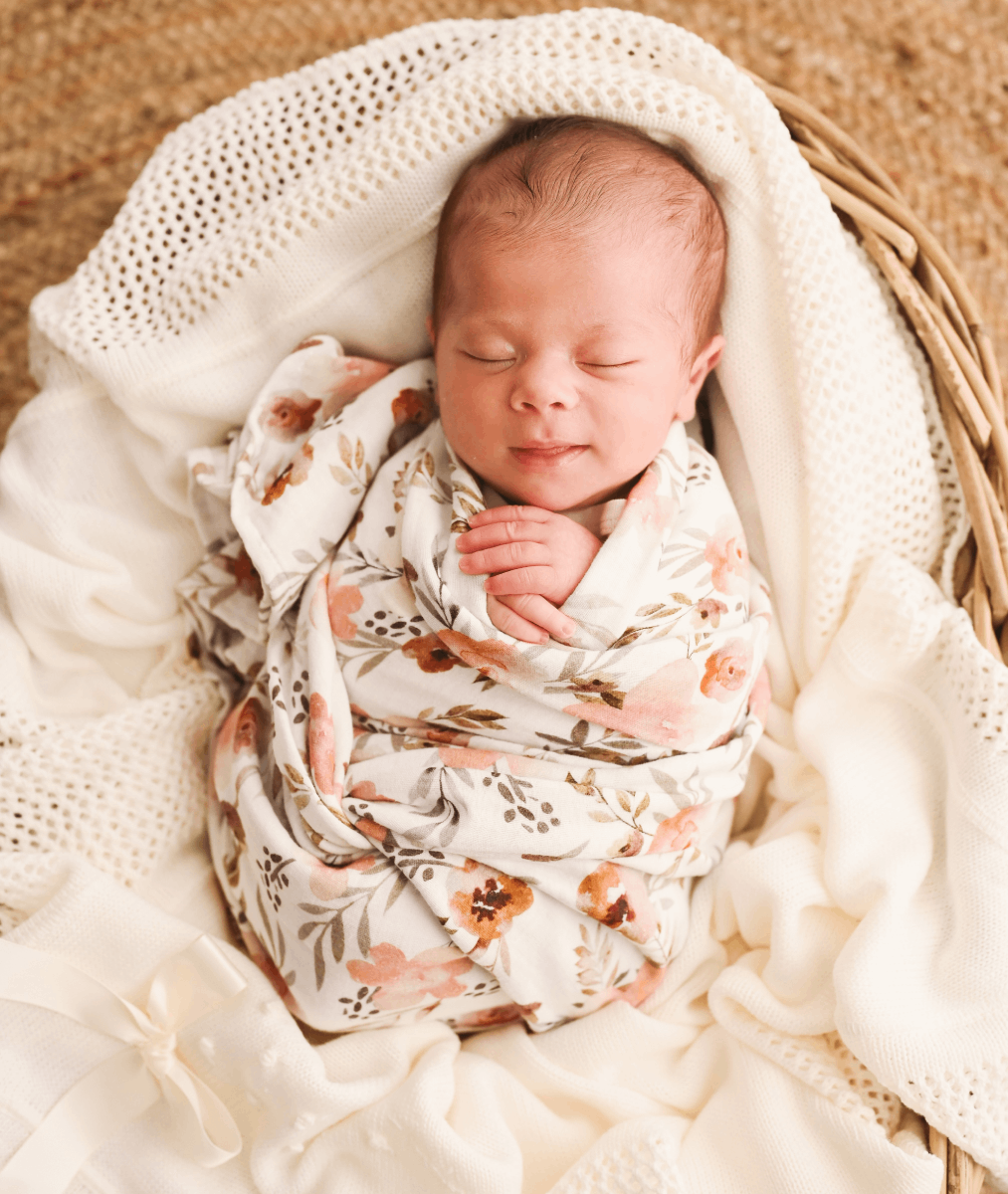 Fralda Swaddle Bebé recém-nascido envolto em manta floral numa cesta sobre mantas brancas