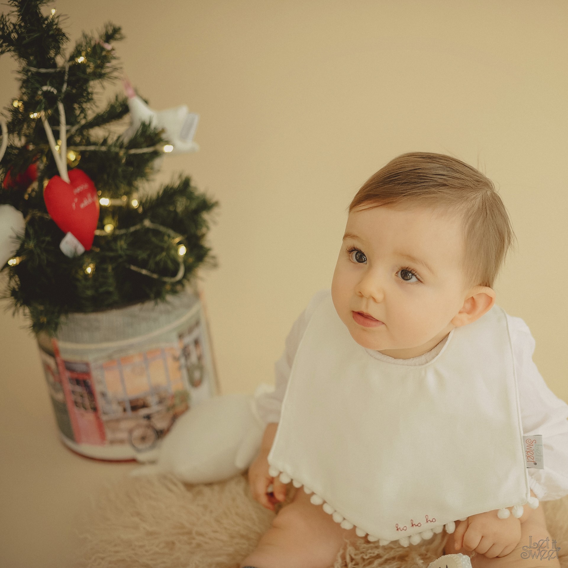 Babete de Natal Bebé com babete branco sentado perto de árvore de Natal decorada