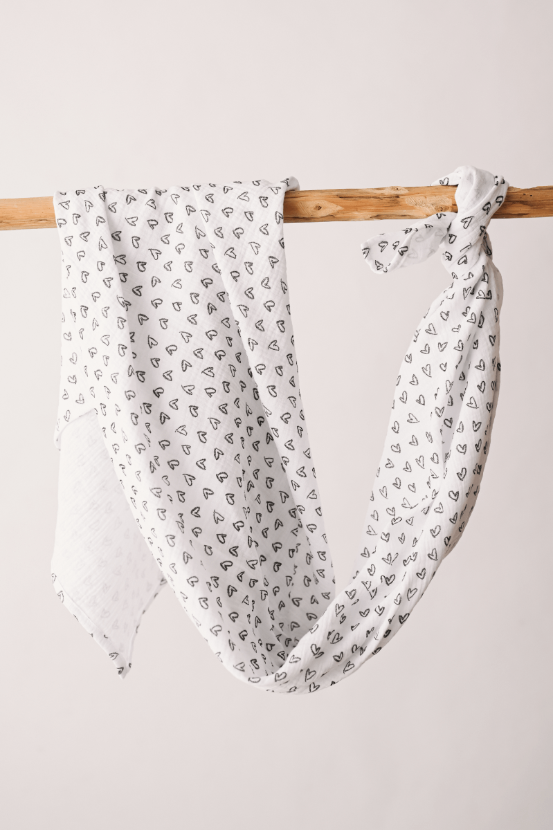 Fralda Swaddle Lenço branco com corações pretos pendurado numa barra de madeira