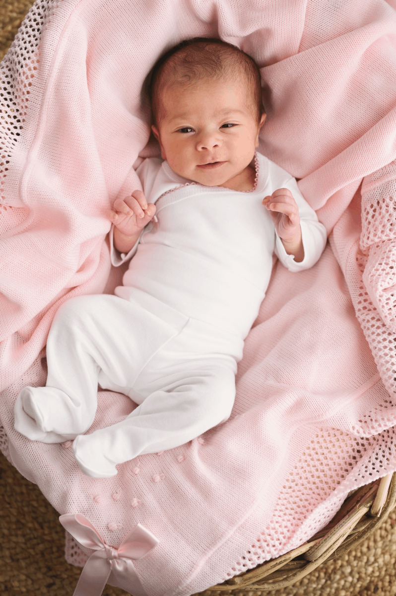 Conjunto de roupinha Bebé recém-nascido em roupinha branca de algodão sobre manta rosa numa cesta