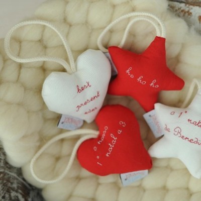 Enfeites de Natal em tecido vermelho e branco com textos bordados, dispostos sobre manta de lã creme