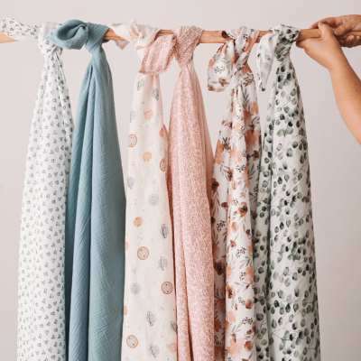 Seis panos leves pendurados num varão de madeira com padrões florais e cores suaves.