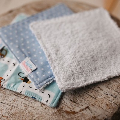 Três panos de tecido de diferentes padrões e texturas sobre mesa redonda de madeira clara.