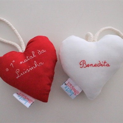 Dois corações de tecido pendurados com cordão, vermelho e branco, com textos bordados.