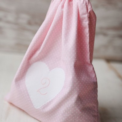 Saco de tecido rosa com cordão e número 2 dentro de coração branco.