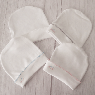 Quatro gorros de bebé brancos com bordados coloridos e etiqueta baby MILES em madeira clara