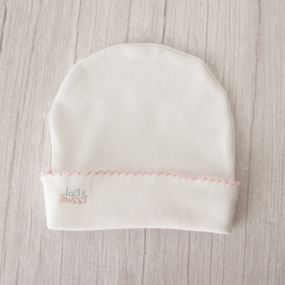 Gorro branco com detalhe rosa e etiqueta 'let it SWEET' sobre madeira clara