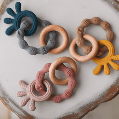 Três mordedores de bebé redondos e coloridos sobre superfície branca com bordas castanhas