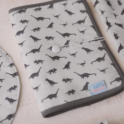 Capa para caderno com padrão de dinossauros em tecido cinzento claro e fecho com botão branco