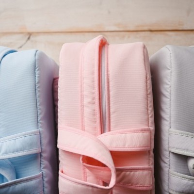 Três mochilas coloridas alinhadas sobre uma mesa de madeira clara