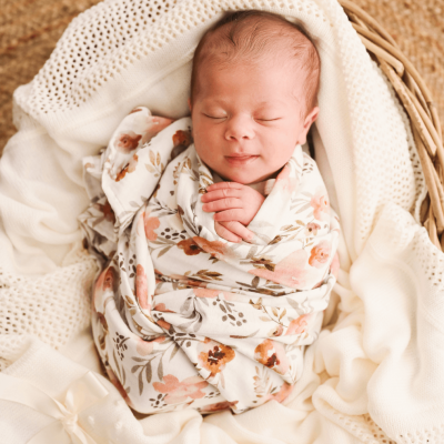 Bebé recém-nascido envolto em manta floral numa cesta sobre mantas brancas